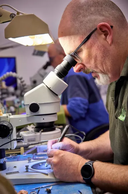A man is inspecting a hearing aid through a microscope